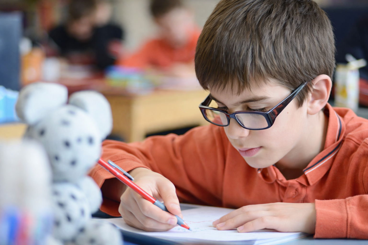 Enfant portant des lunettes écrivant soigneusement dans un cahier pendant un exercice scolaire.