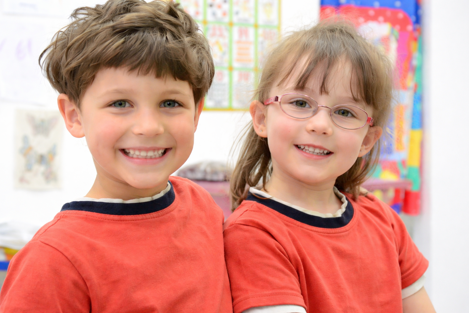 Deux enfants souriants côte à côte regardant la caméra dans un environnement scolaire.